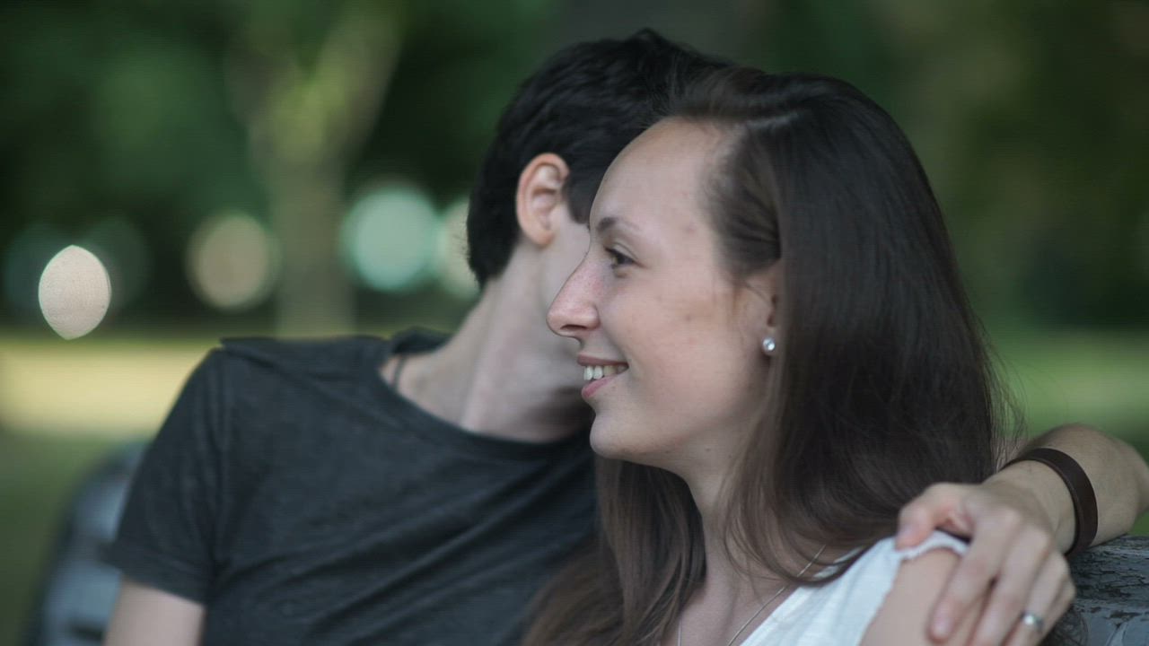 LGTBQ women kiss and talk on park bench.