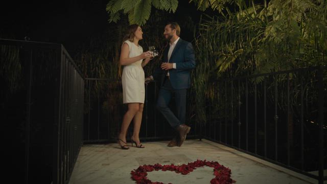 A young couple dressed in elegant attires take a selfie on the balcony at night.