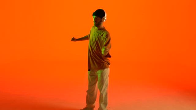 A young man with a beanie and headphones dancing over an orange background.