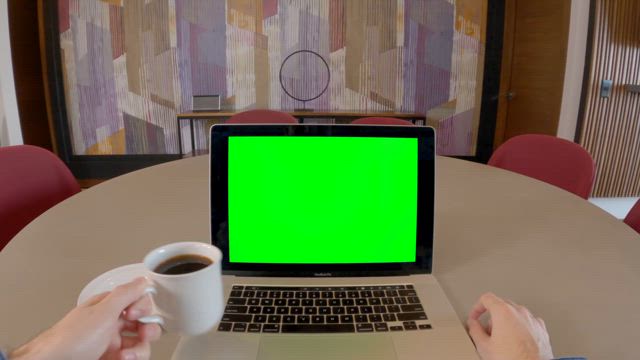 On a round table the hands of a young man start typing on a modern laptop computer with a green screen.