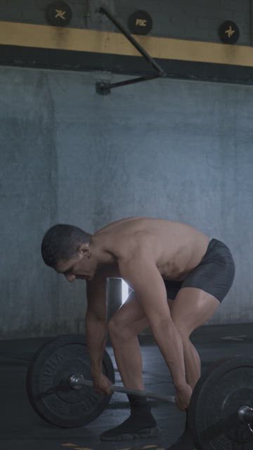 A young muscular man training his strength and overall fitness by lifting the gym bar.