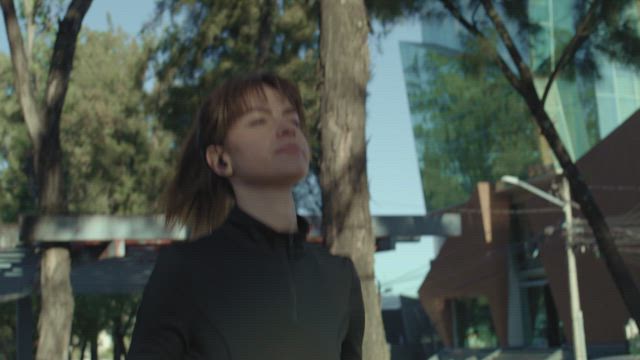 A young woman wearing black sportswear runs through the park in the morning.