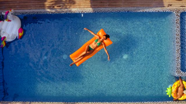 Aerial view of a young woman wearing a colorful bikini enjoying the swimming pool over an orange floaty.