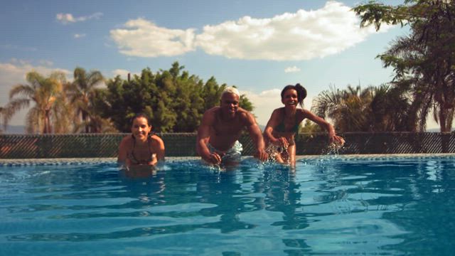 Three young carefree individuals jump to the swimming pool on a summer sunny day in slow motion creation a refreshing splash.