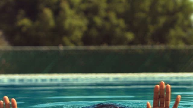 A young African American woman slowly breaking the swimming pool surface with her head on a sunny day.